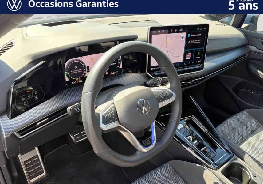 Vue intérieure du poste de conduite de la Volkswagen Golf 1.5 eHybrid 2025, volant sport cuir et écran tactile central visible.