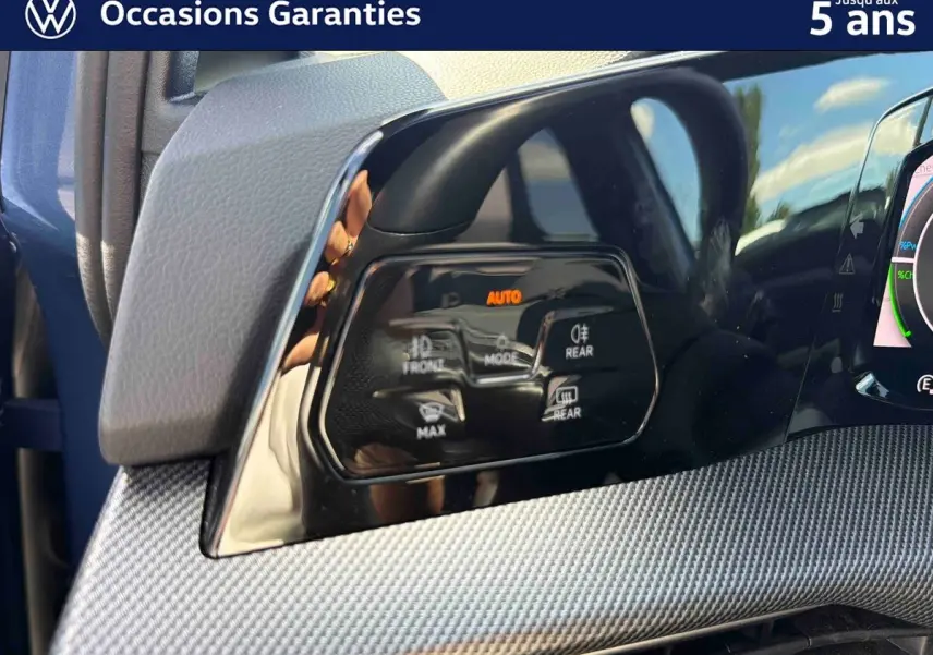 Détail du tableau de bord côté gauche de la Volkswagen Golf 1.5 eHybrid 2025 bleu, avec commandes d’éclairage et finition texturée.