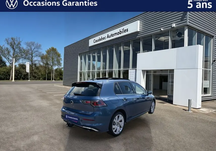 Vue 3/4 arrière droite d'une Volkswagen Golf 1.5 eHybrid 272 DSG6 bleu métallisé avec toit panoramique et attelage rabattable.