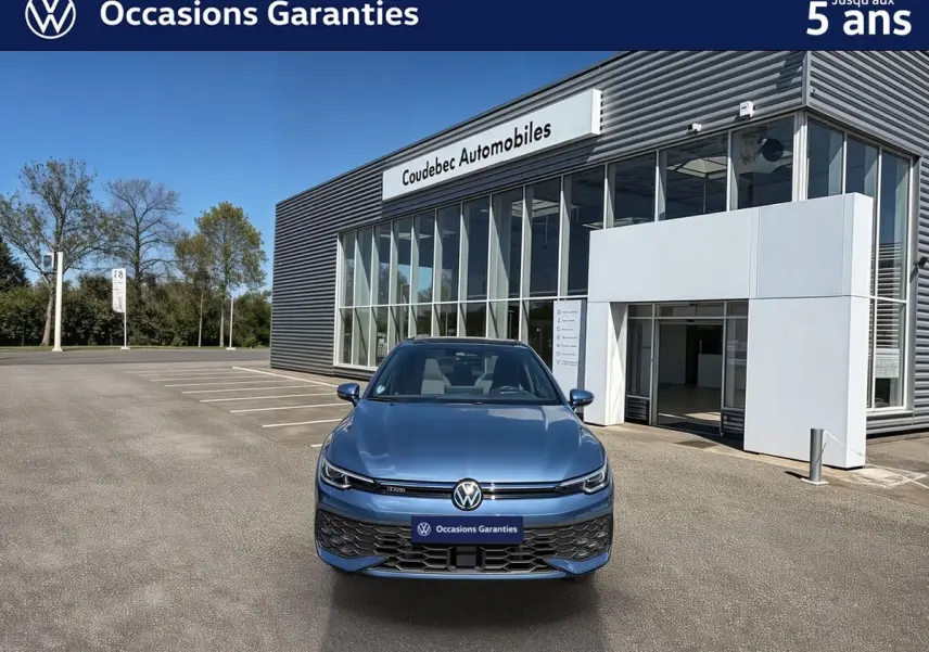 Vue avant d'une Volkswagen Golf 1.5 eHybrid 272 DSG6 bleue métallisée, avec calandre et logo VW visibles, devant un showroom.