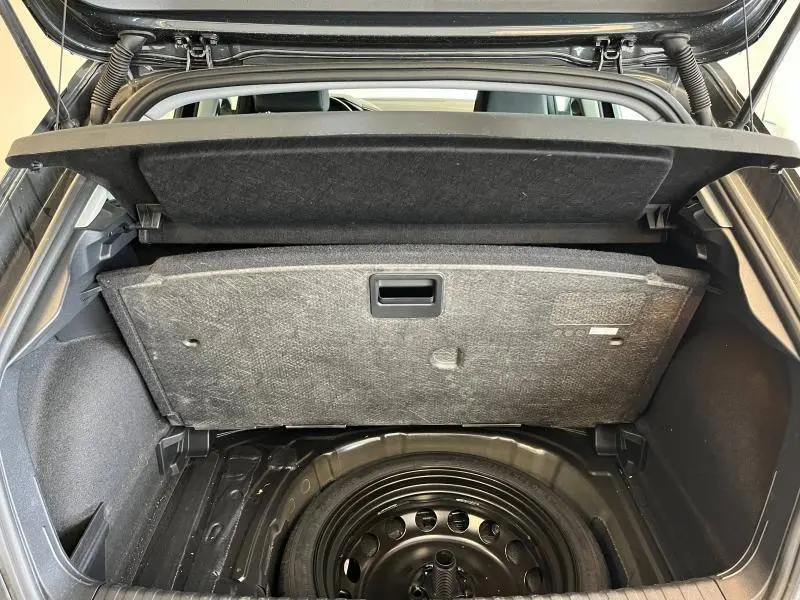 Coffre ouvert d'une Audi A1 Sportback noir Mythic, vue arrière montrant la roue de secours sous le plancher.