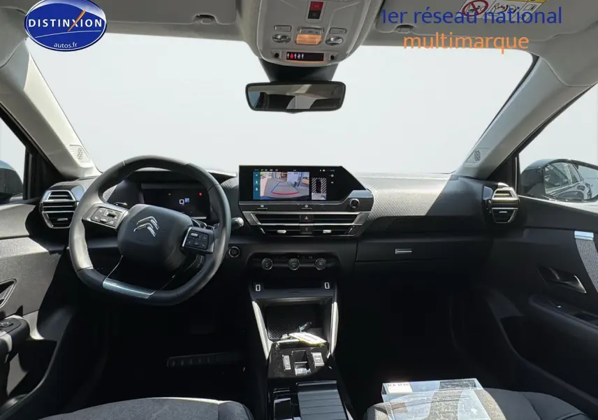 Intérieur de la Citroën C4 2025 vu de face, tableau de bord noir avec écran tactile et volant cuir.