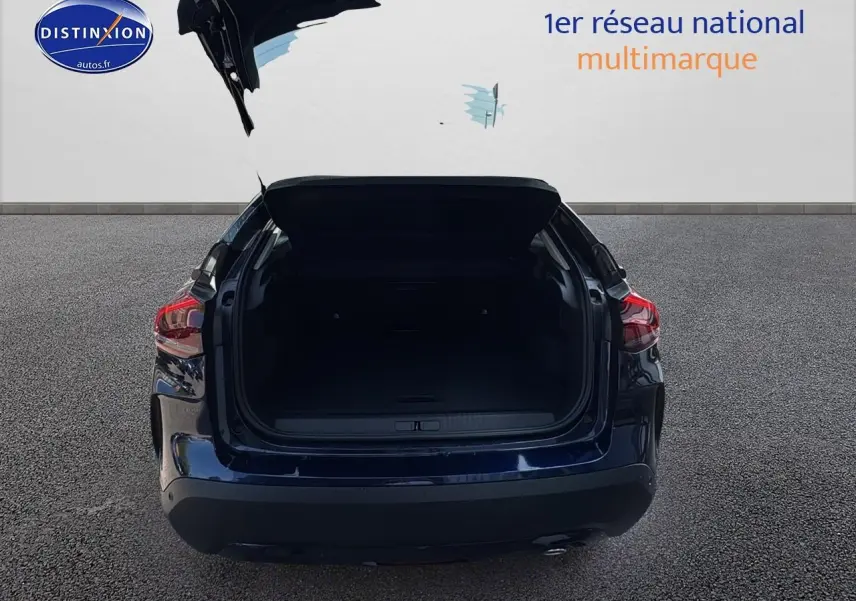 Vue arrière d'une Citroën C4 bleu eclipse avec coffre ouvert sur sol gris.
