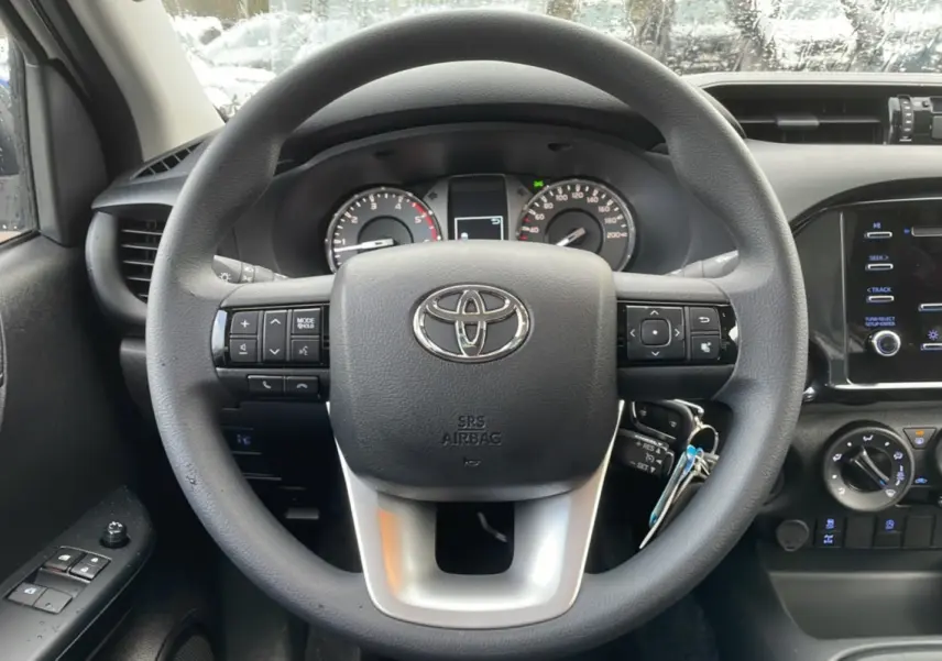 Vue rapprochée du volant noir du Toyota Hilux 2024 avec commandes intégrées et tableau de bord visible.