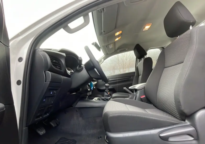 Intérieur du Toyota Hilux 4x4 2024 en vue latérale côté conducteur, sièges noirs et tableau de bord visible.