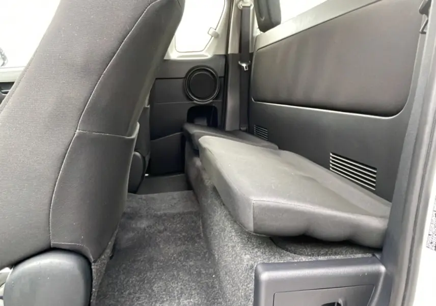 Vue intérieure arrière côté droit du Toyota Hilux 4x4 2024 blanc, montrant la banquette rabattue et les sièges noirs.