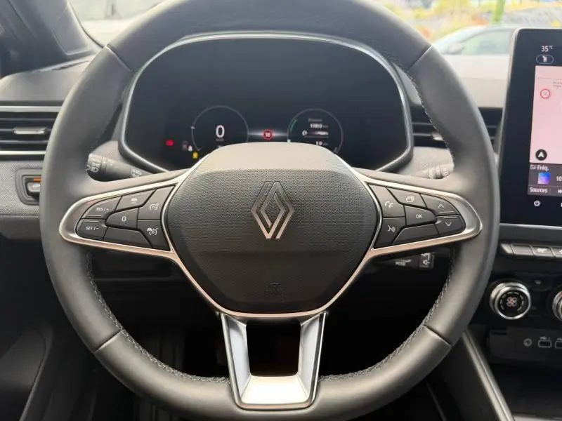 Vue rapprochée du volant multifonction gris et noir de la Renault Clio 1.0 Eco-G 2025 avec tableau de bord numérique en arrière-plan.