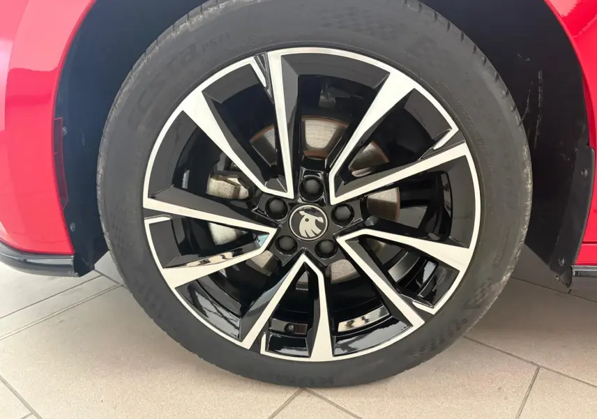Gros plan sur la jante noire et argentée du côté gauche d'une Skoda Fabia rouge Velvet avec logo au centre.
