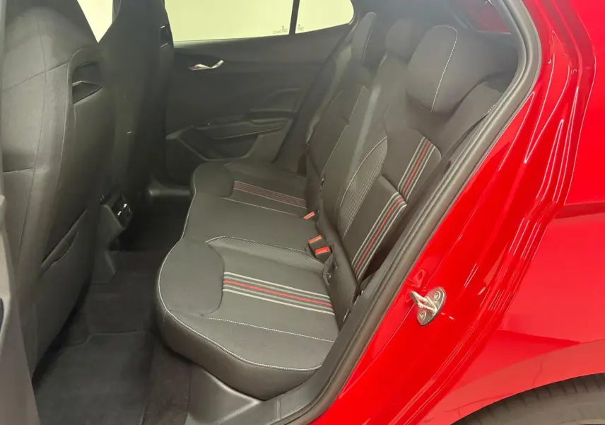 Vue intérieure côté gauche des sièges arrière noirs avec surpiqûres rouges, porte ouverte sur carrosserie rouge velvet.