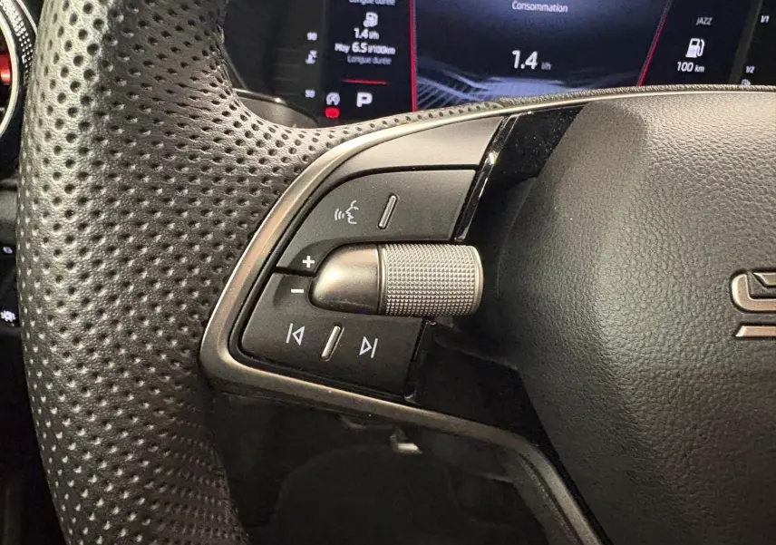 Gros plan sur les commandes gauche du volant perforé d’une Skoda Fabia 2025, avec écran numérique en arrière-plan.