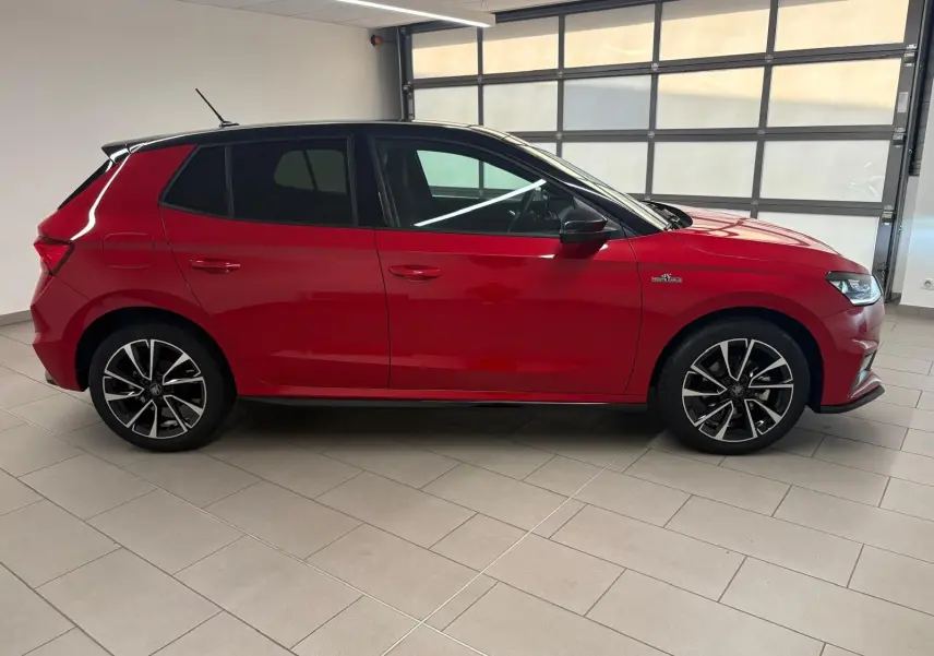 Vue latérale droite d'une Skoda Fabia 2025 rouge Velvet avec toit noir et jantes alliage noires, en intérieur showroom.