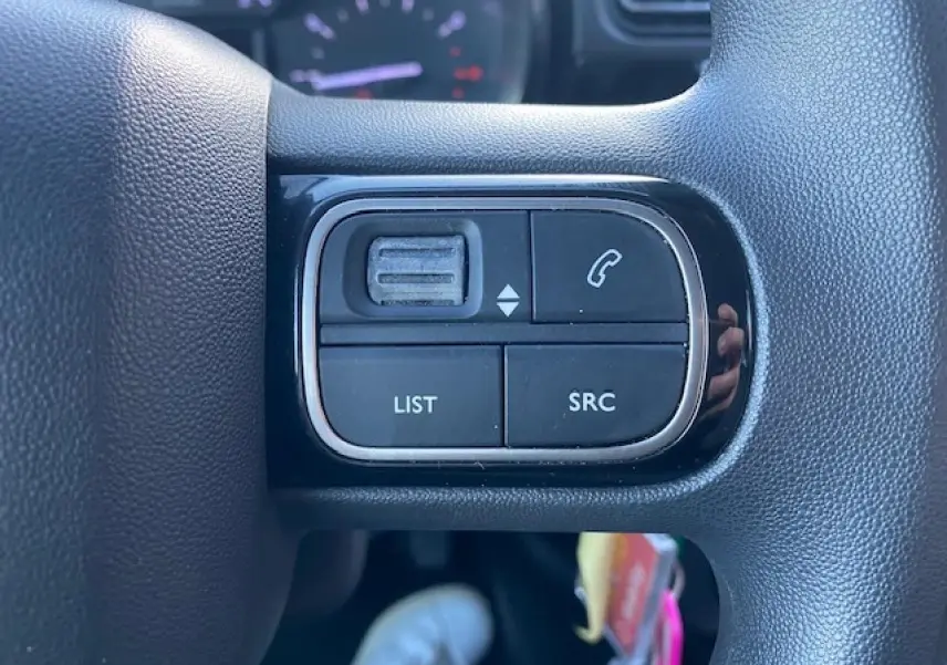Gros plan sur les commandes audio au volant d'une Citroën C3 Shine 2023 noir toit rouge, avec boutons list, SRC et appel.