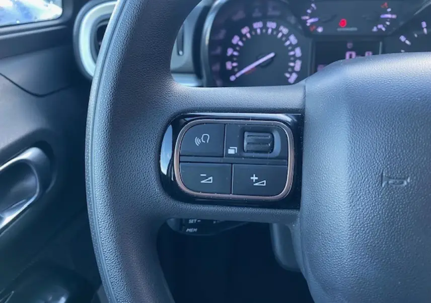 Gros plan sur le volant côté gauche de la Citroën C3 Shine 2023, montrant les commandes audio intégrées.