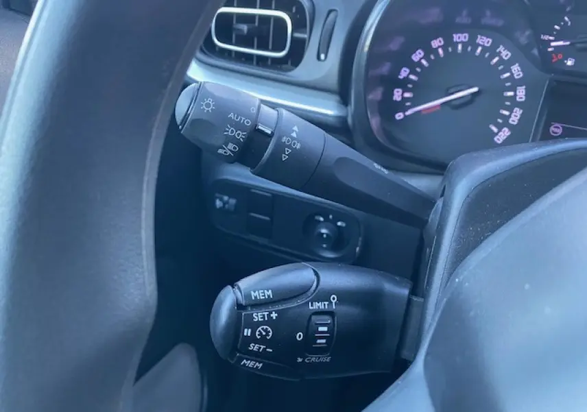 Gros plan sur les commandes au volant de la Citroën C3 Shine 2023, avec tableau de bord et levier de régulateur de vitesse visibles.