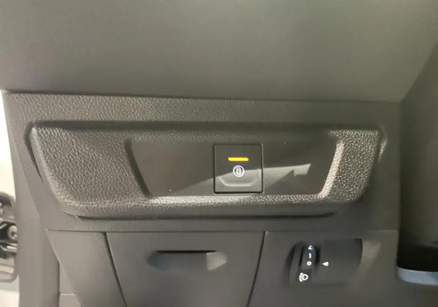 Gros plan sur le bouton de frein de stationnement électrique dans l’habitacle d’une Dacia Sandero blanc glacier.