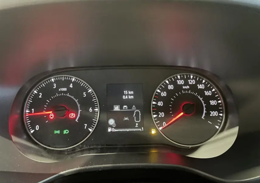 Vue rapprochée du tableau de bord numérique et analogique du Dacia Sandero blanc, affichant 15 km au compteur.