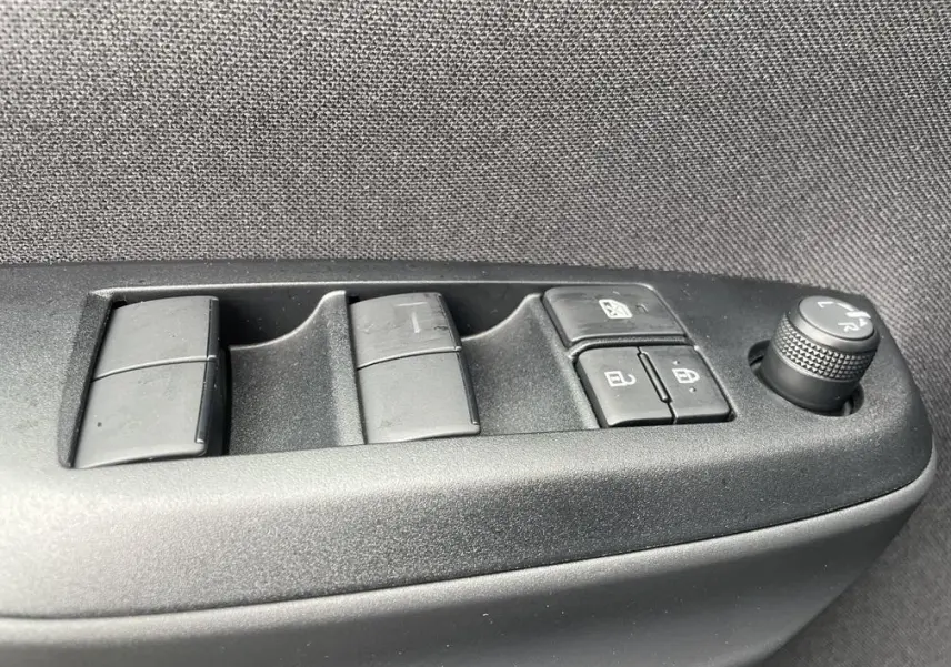 Gros plan sur les commandes de lève-vitres et réglage des rétroviseurs côté conducteur d'une Toyota Yaris Cross gris clair.