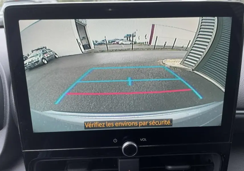 Vue arrière via caméra de recul du Toyota Yaris Cross gris clair, avec lignes de guidage bleues et rouges visibles à l'écran.