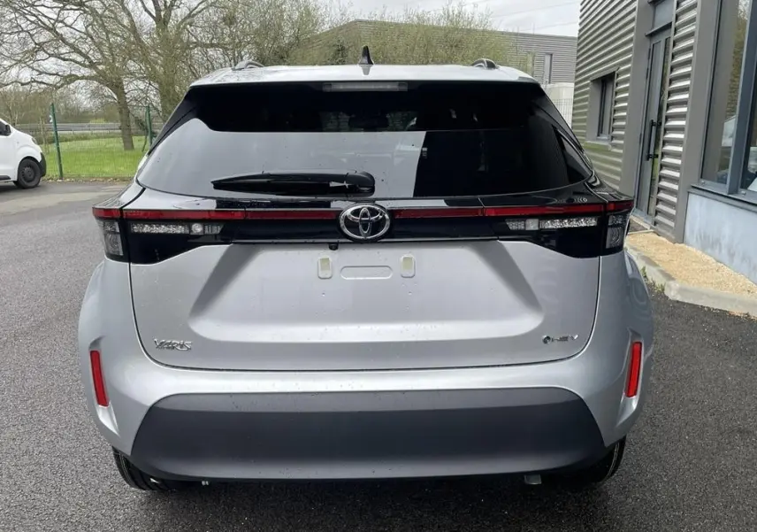 Vue arrière d'une Toyota Yaris Cross gris clair avec feux arrière reliés par une bande noire brillante.