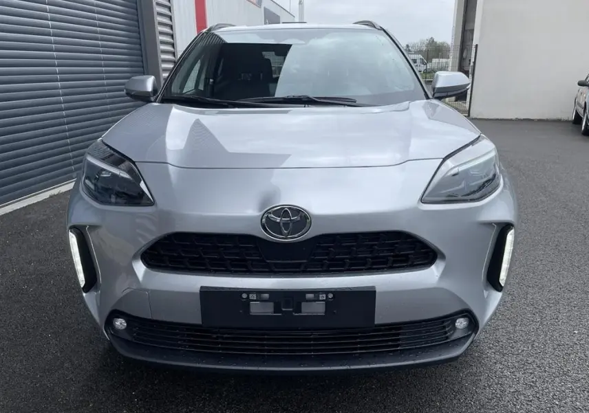 Vue frontale d'une Toyota Yaris Cross gris clair avec calandre noire et feux diurnes verticaux allumés.