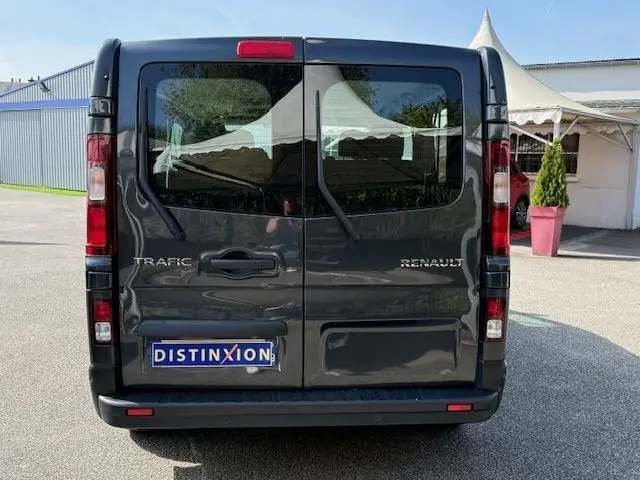 Vue arrière d'un Renault Trafic Combi gris comète, portes battantes fermées avec logo et plaque Distinxion visible.