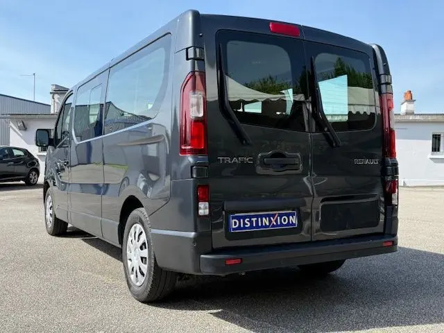 Vue 3/4 arrière droite d’un Renault Trafic Combi gris comète 2022 avec hayon double et logo distinctif sur parking.
