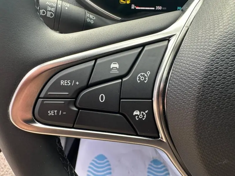 Gros plan sur les commandes multifonctions du volant côté gauche d’une Renault Clio rouge Flamme 2025.