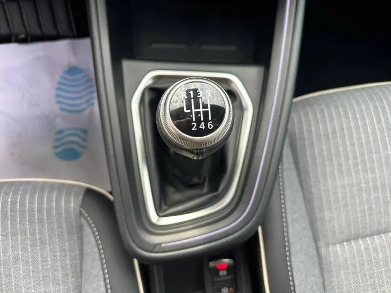 Gros plan sur le levier de vitesses manuel noir entouré de garniture grise, entre les sièges tissu gris de la Renault Clio rouge.