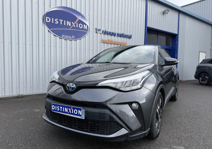 Toyota C-HR 1.8 hybrid gris atlas vu en 3/4 avant droit devant un bâtiment commercial.