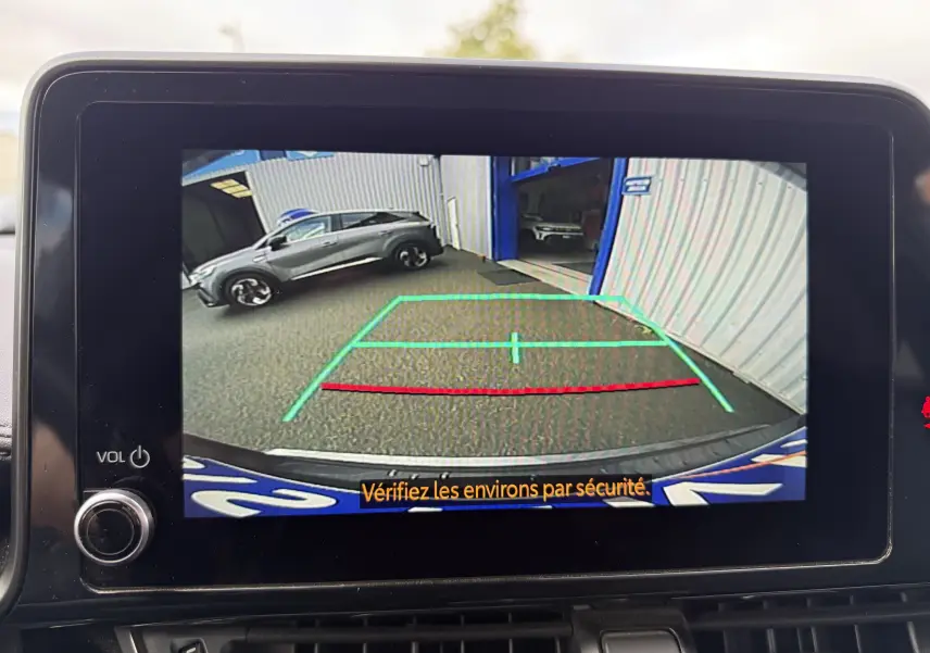 Vue caméra de recul montrant un Toyota C-HR gris atlas garé côté gauche devant un bâtiment industriel.