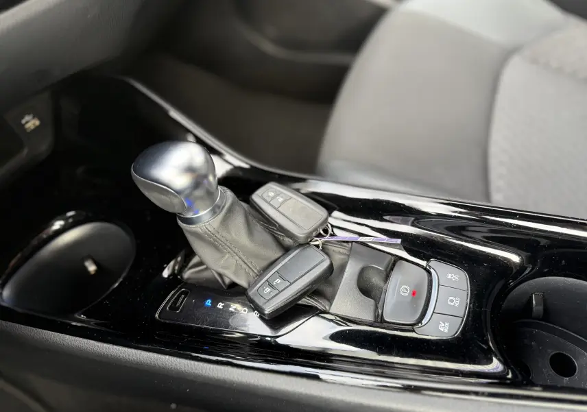 Gros plan sur la console centrale noire brillante du Toyota C-HR 1.8 hybrid avec levier de vitesse et clés posées.