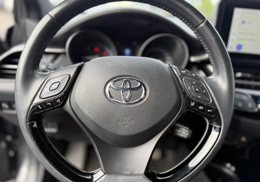 Vue rapprochée du volant noir du Toyota C-HR 1.8 hybrid 2023 avec commandes intégrées et logo central chromé.