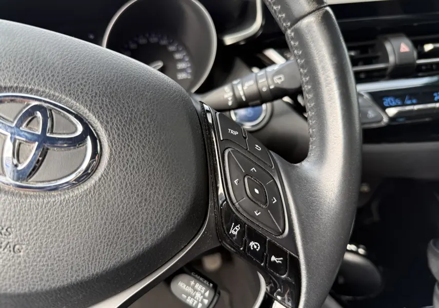 Gros plan sur le volant noir du Toyota C-HR 2023, montrant les commandes multifonctions côté droit et le logo Toyota central.