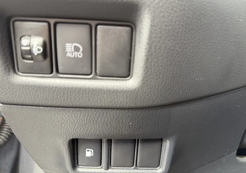 Détail intérieur montrant les boutons de réglage des phares et de l'ouverture du bouchon de carburant du Toyota C-HR hybride.
