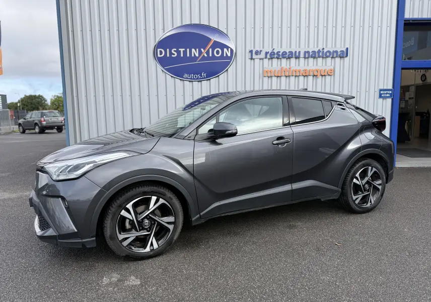 Toyota C-HR 1.8 hybrid gris atlas vu de profil côté gauche, avec jantes alliage bicolores et lignes sculptées.