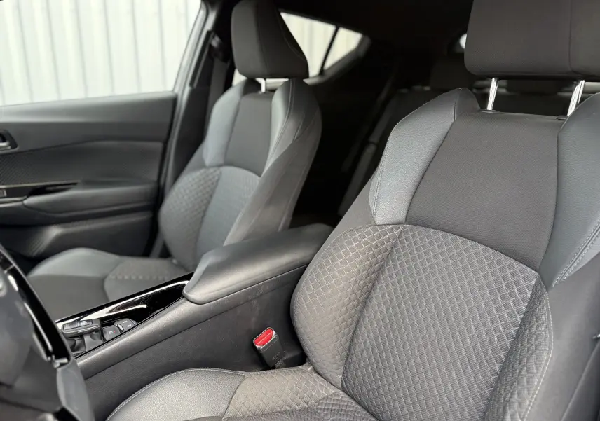 Vue intérieure rapprochée des sièges avant gris tissu du Toyota C-HR 1.8 hybrid 2023 avec accoudoir central noir.