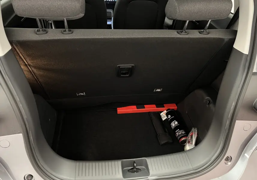 Coffre ouvert vu de l'arrière d'une Dacia Spring blanche, avec triangle de signalisation et extincteur visibles.