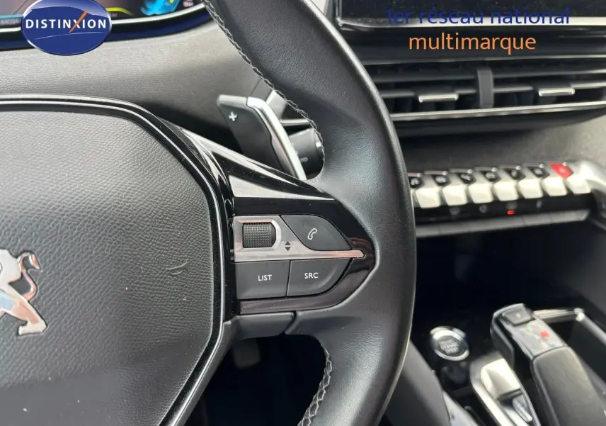 Gros plan sur le volant cuir noir du Peugeot 3008 hybride 2022 avec commandes intégrées et levier de vitesse visible.