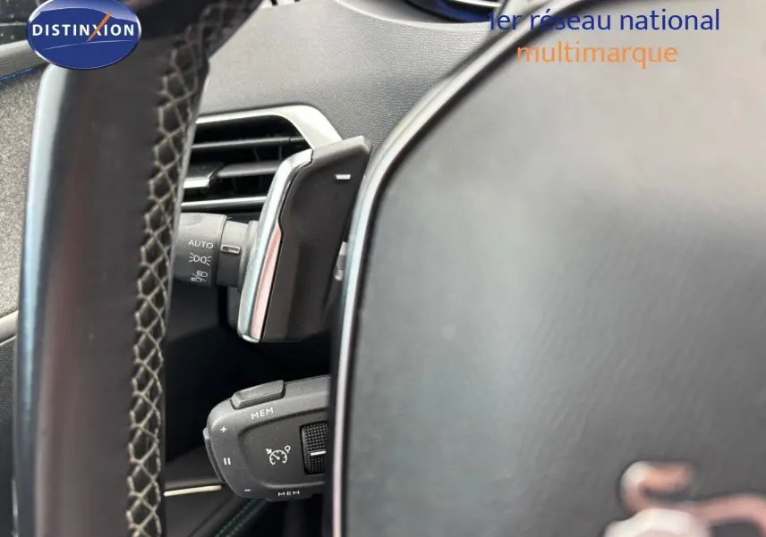 Gros plan sur la commande de régulateur de vitesse derrière le volant d’un Peugeot 3008 bleu Celebes hybride rechargeable.