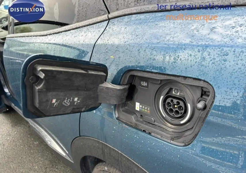 Prise de recharge ouverte côté gauche sur Peugeot 3008 hybride rechargeable bleu Célèbes sous la pluie.