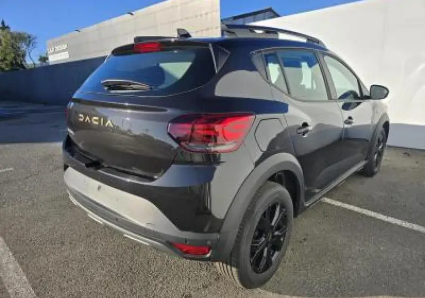 Vue 3/4 arrière droite d'une Dacia Sandero Stepway 2025 noir nacré avec jantes aluminium noires et barres de toit.
