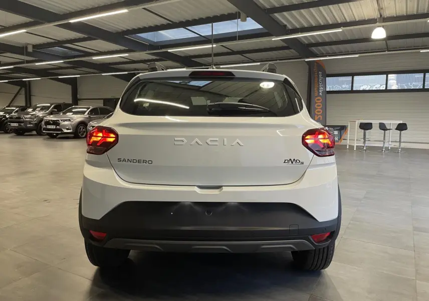 Vue arrière d'une Dacia Sandero TCe 90 Stepway blanche Glacier avec feux allumés dans un showroom.