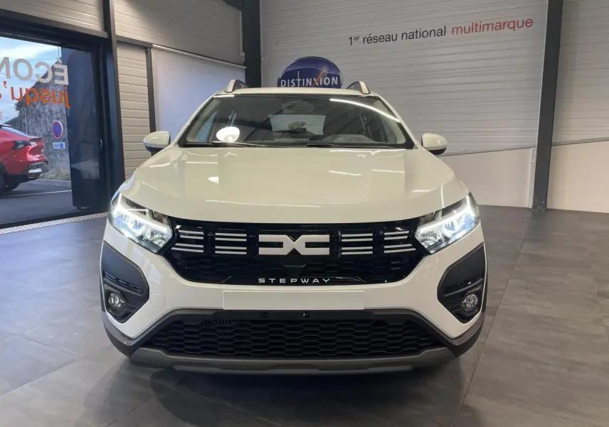 Vue de face d'une Dacia Sandero Stepway blanche Glacier avec calandre noire et signature lumineuse LED allumée.