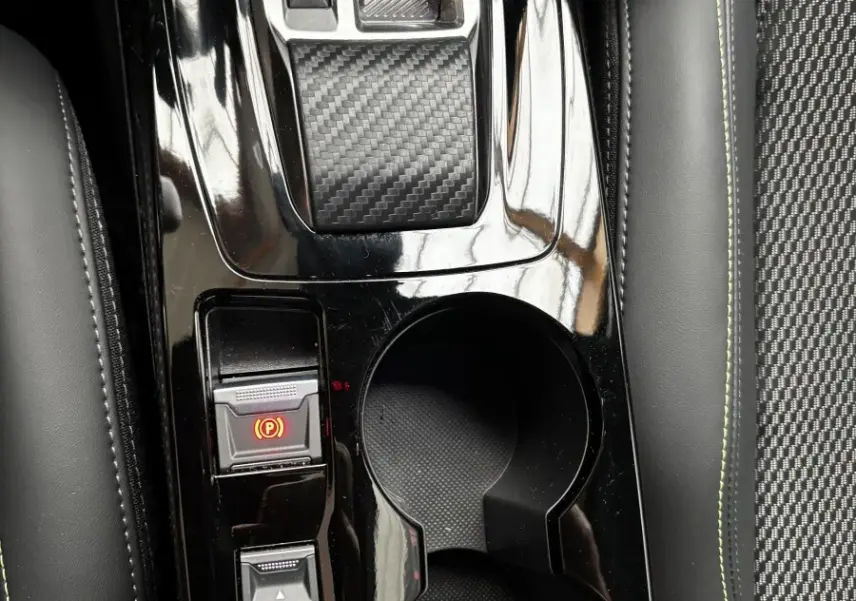 Vue rapprochée de la console centrale noire brillante avec sélecteur de boîte auto et porte-gobelets dans Peugeot 208 Hybrid 110 GT.
