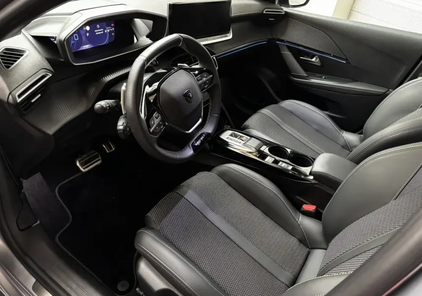 Intérieur avant droit de la Peugeot 208 Hybrid 110 e-DCS6 GT 2025, sièges noirs, volant cuir alu et tableau de bord numérique.