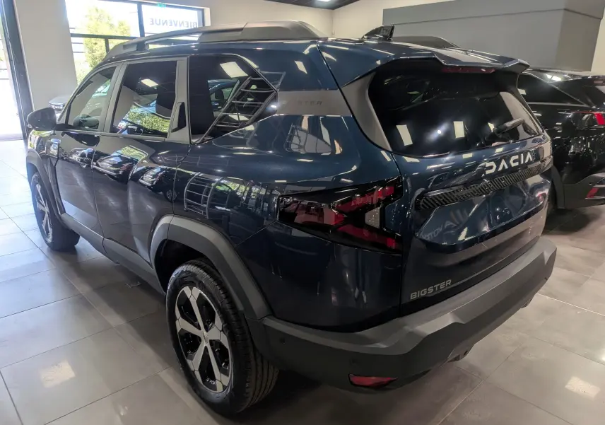 Vue 3/4 arrière droite du Dacia Bigster bleu indigo avec logo et feux arrière distinctifs en intérieur showroom.