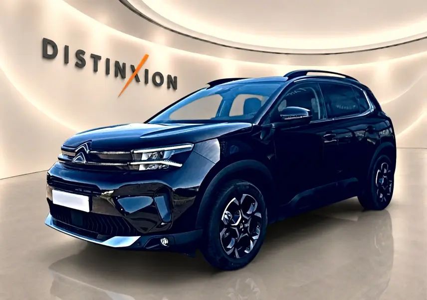 Citroën C5 Aircross noir en 3/4 avant droit, avec barres de toit et jantes alu distinctives dans un showroom lumineux.