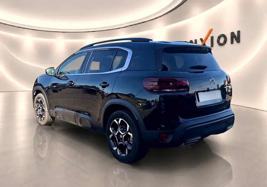 Vue 3/4 arrière droite d'un Citroën C5 Aircross noir avec jantes alu et barres de toit visibles en intérieur.