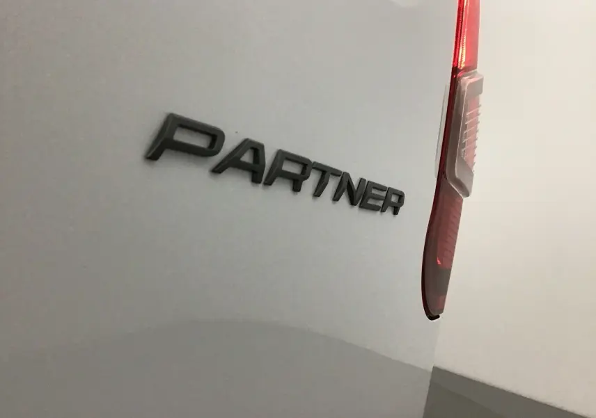 Gros plan sur l'arrière droit blanc du Peugeot Partner 2025, mettant en valeur le logo "PARTNER" et le feu arrière vertical.