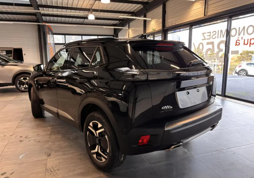 Vue 3/4 arrière droite d'un Peugeot 2008 noir brillant en showroom avec jantes alliage bi-ton et feux arrière LED griffés.